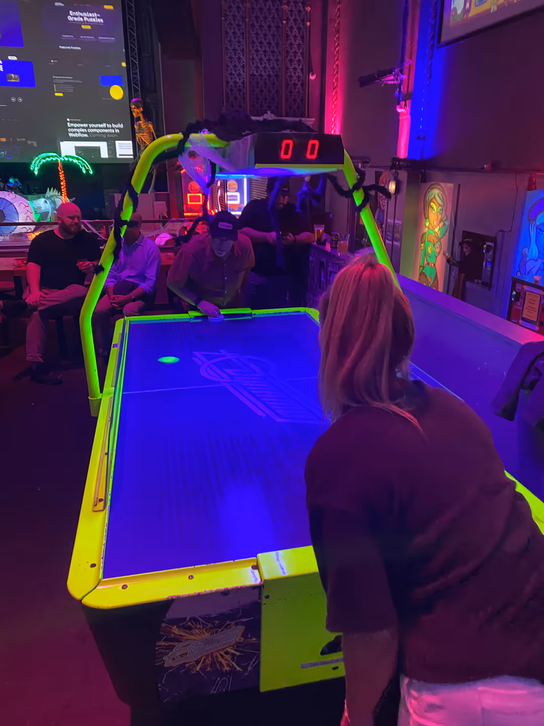 Teammates playing air hockey at an arcade